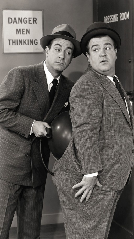 A black-and-white photo of comedians Bud Abbott and Lou Costello; Abbott holds a balloon behind Costello's back near a sign that reads "DANGER MEN THINKING".