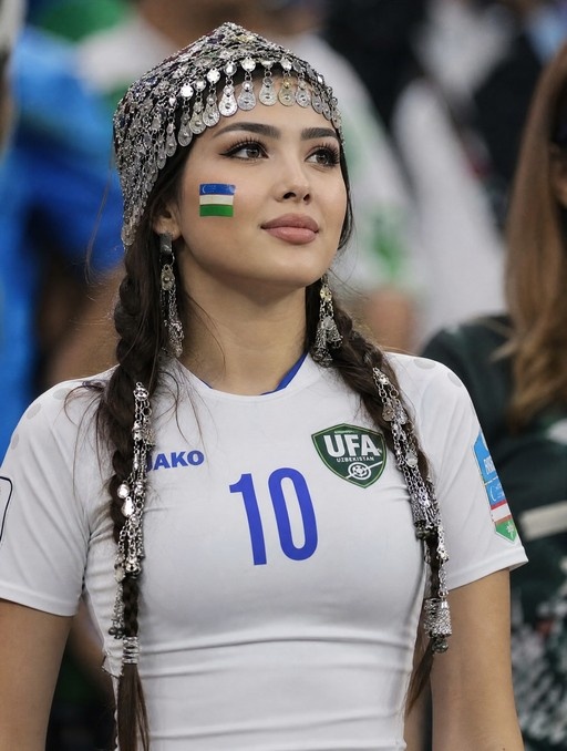 Young woman wearing a white soccer jersey and traditional silver headdress with Uzbekistan flag painted on her cheek
