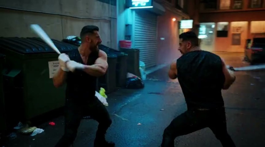 Two muscular men in black tank tops fight with baseball bats in a dark alley until a gothic woman with a giant bat appears to challenge them.