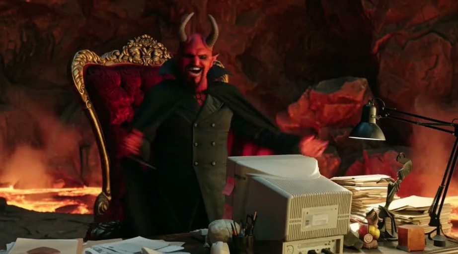 A red-skinned demon with horns sits at a desk in a fiery office, typing on a computer that displays "Access Denied".
