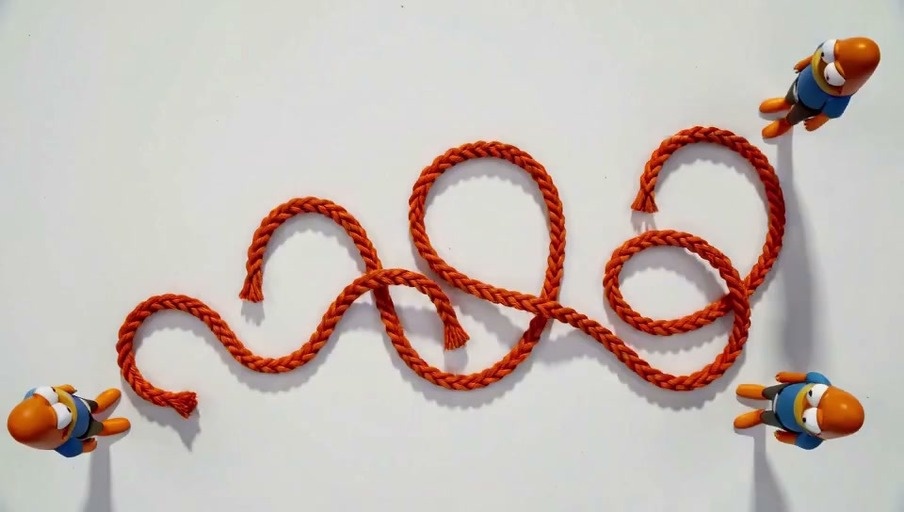 A top-down view of small orange-skinned cartoon figures in blue shirts weaving a thick orange rope into the shape of text on a white surface.