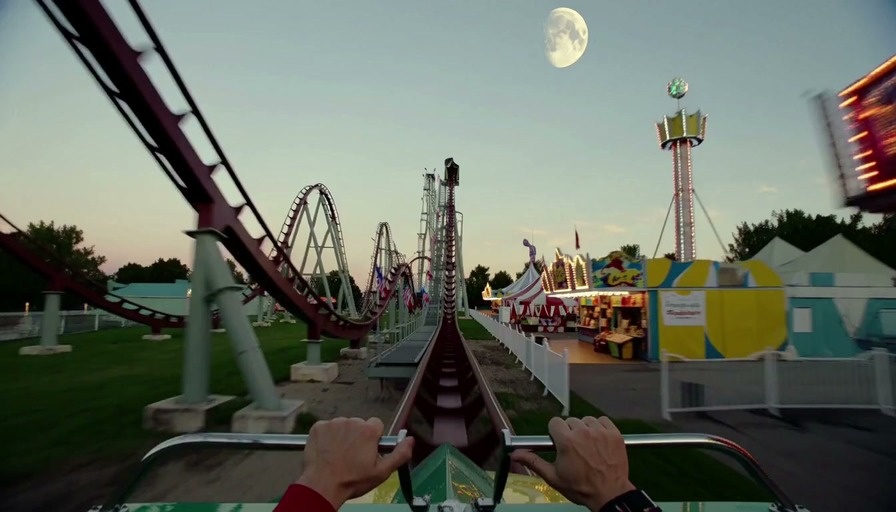 A first-person view from a rollercoaster car moving through an amusement park at dusk, then entering a grand ballroom lined with carousel horses.