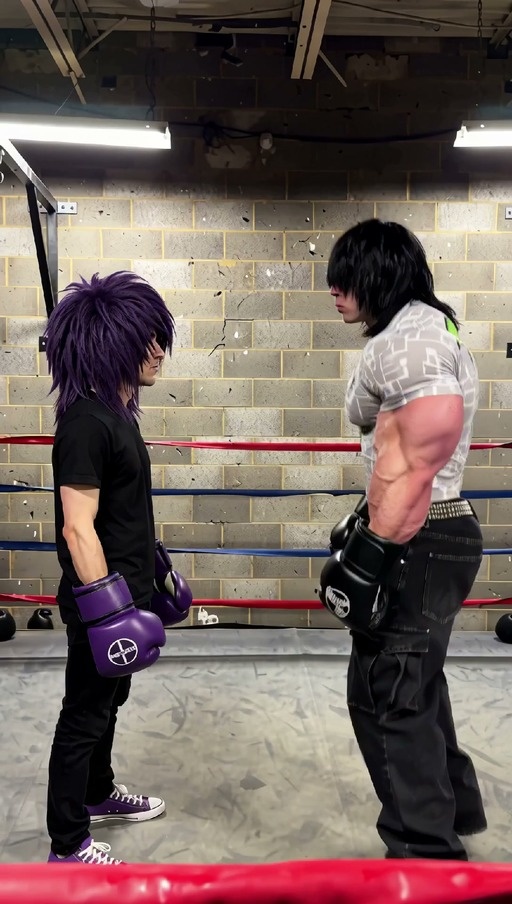 A skinny man with purple hair and boxing gloves stands in a ring while a muscular man with black hair throws punches, eventually crashing through the brick wall behind him.